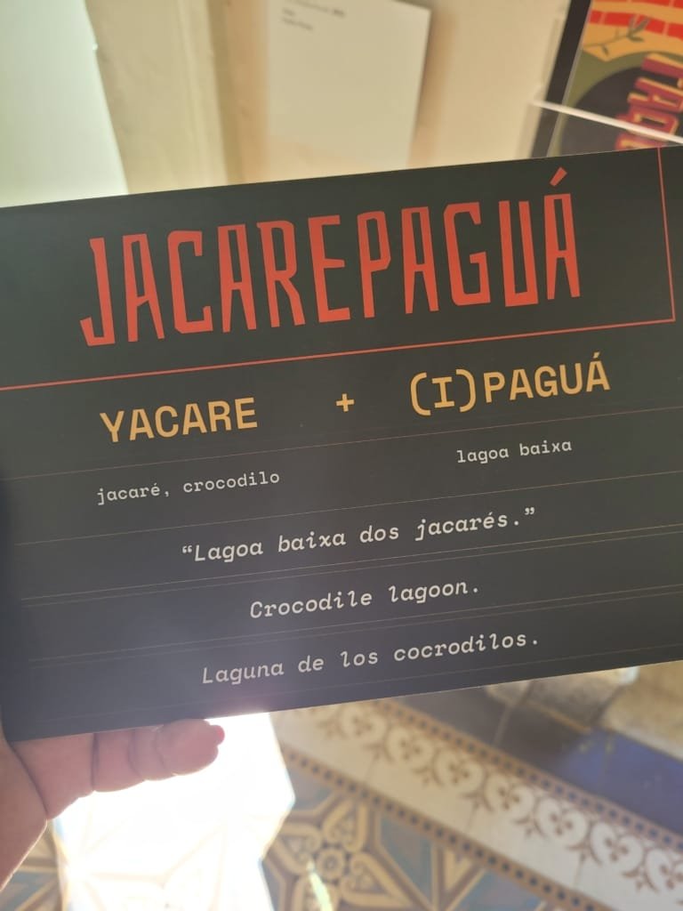 Parque Natural Municipal da Gávea — placa explicativa sobre a origem do nome “Jacarepaguá”, mostrando sua tradução e significado histórico em português, inglês e espanhol dentro do Museu da Cidade do Rio de Janeiro.