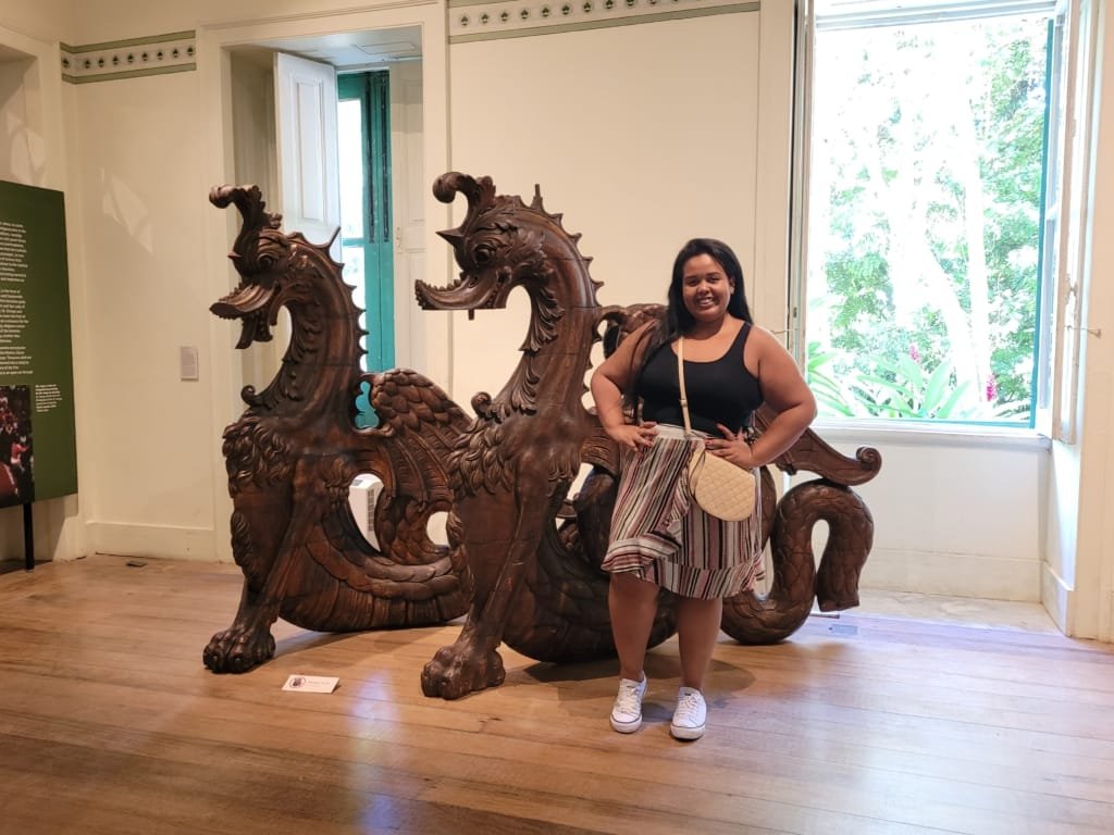 Parque Natural Municipal da Gávea — visitante posa ao lado de uma escultura de dragões em madeira no interior do Museu da Cidade, destacando o acervo artístico e histórico do local.