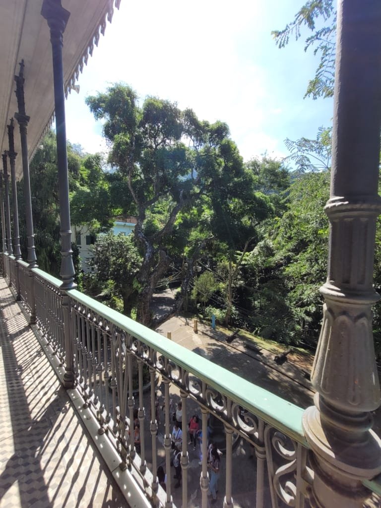 Parque Natural Municipal da Gávea — vista da varanda histórica do Museu da Cidade, mostrando árvores exuberantes, detalhes arquitetônicos do prédio e visitantes apreciando o ambiente natural da Gávea.