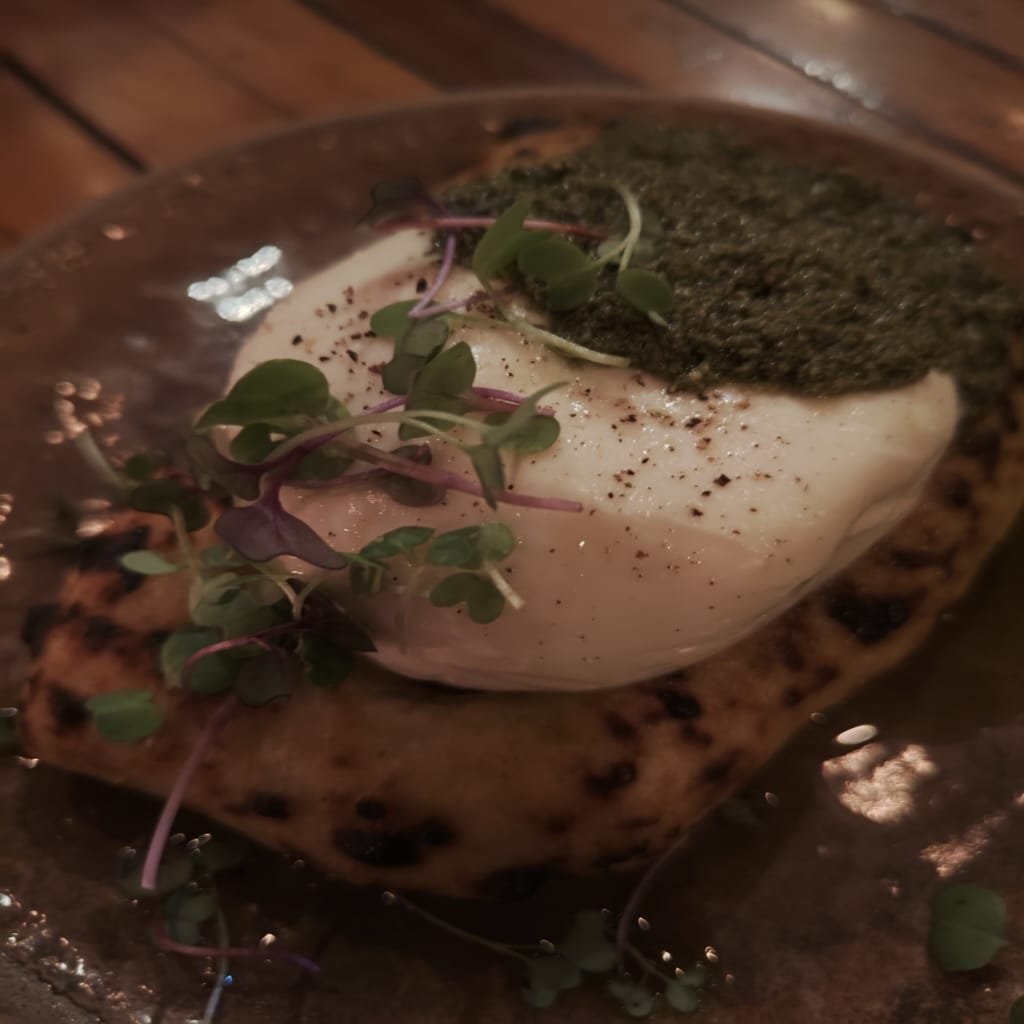 Fresh burrata topped with basil pesto and served on grilled artisanal bread, garnished with microgreens — a popular starter at Ella Pizzaria.