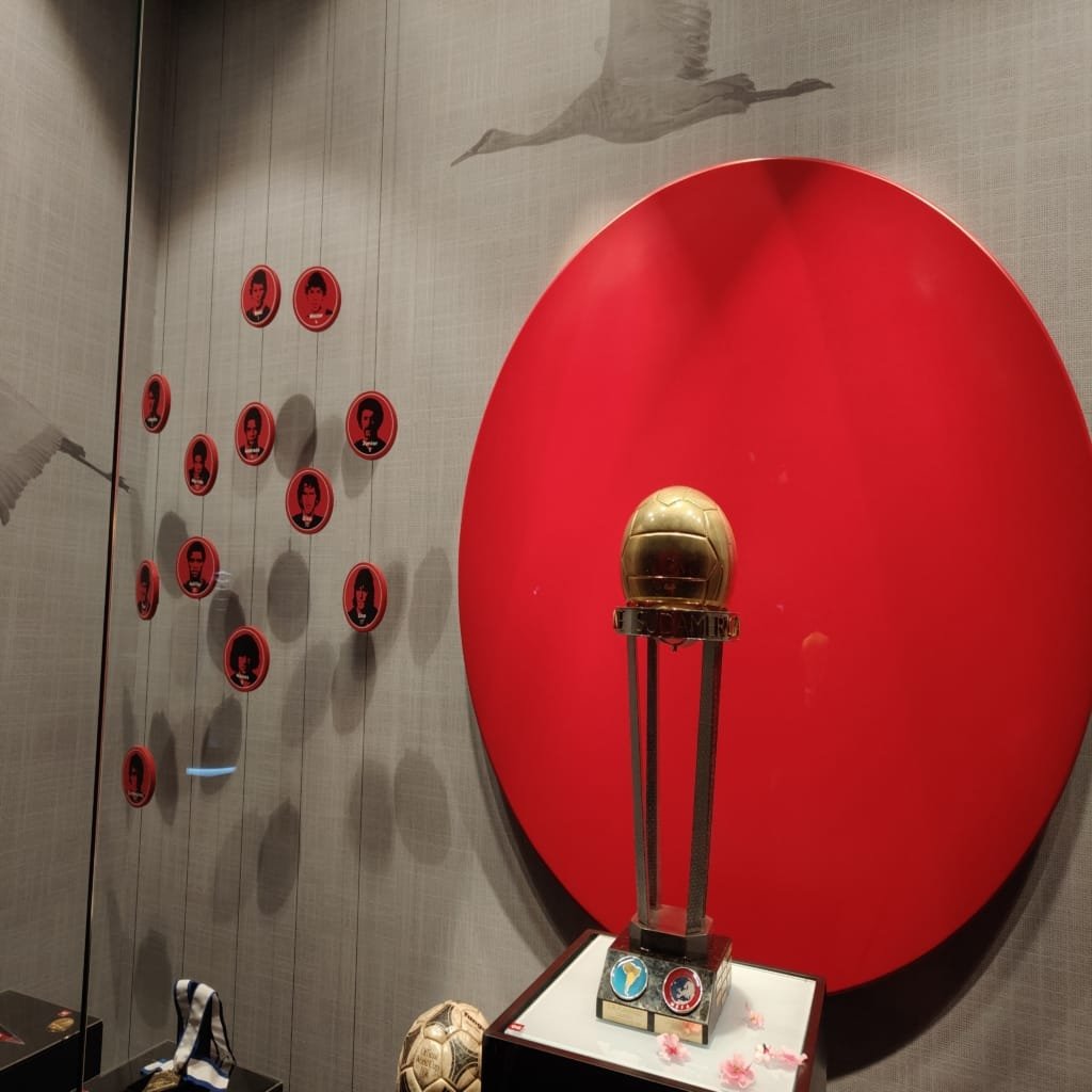 Troféu dourado da Copa Sul-Americana em vitrine do Museu do Flamengo, com fundo vermelho e homenagens aos jogadores.