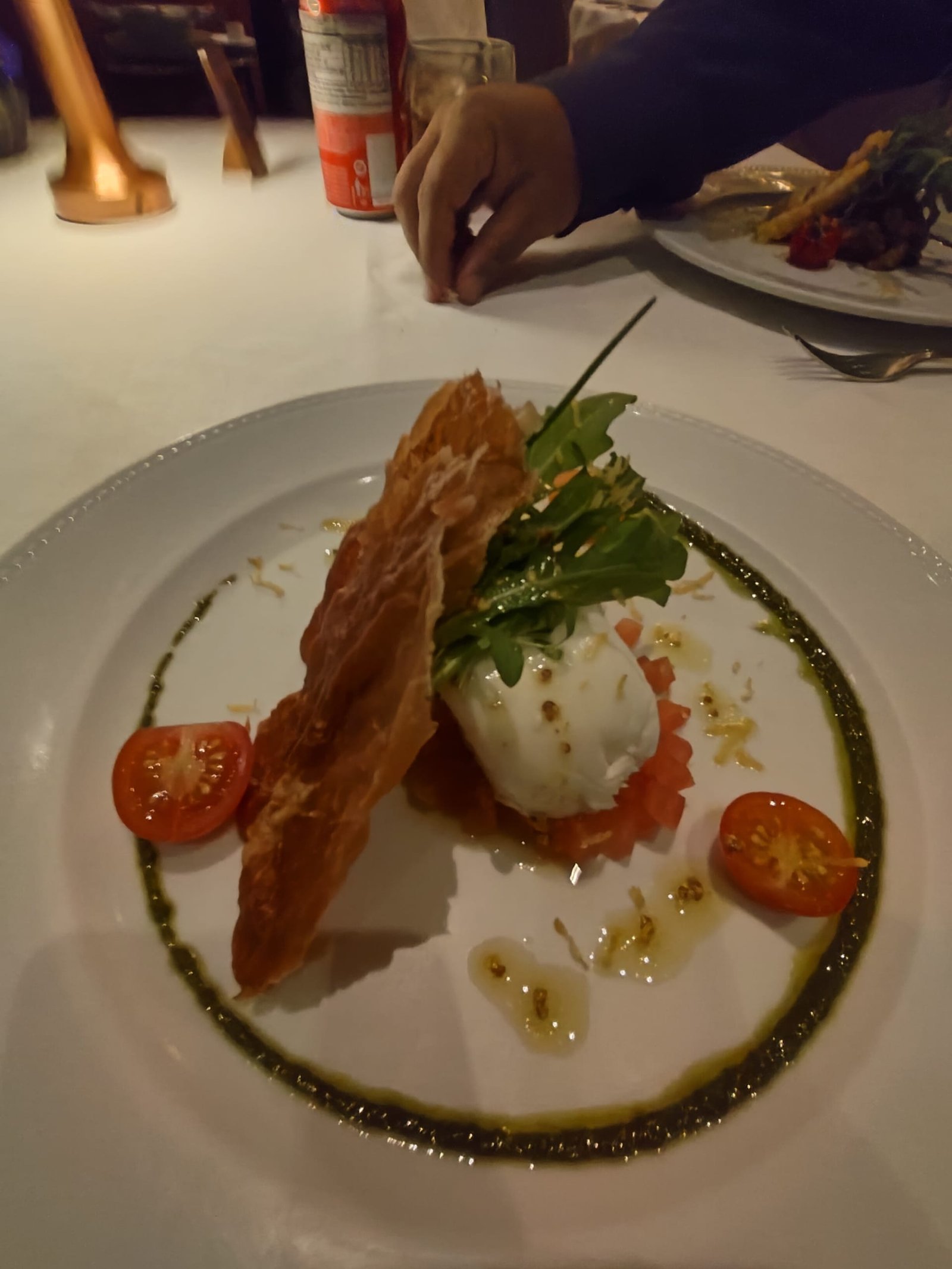 Entrada refinada servida no Restaurante Terraço Itália em São Paulo com burrata, rúcula, tomate cereja e massa crocante decorada com azeite e pesto