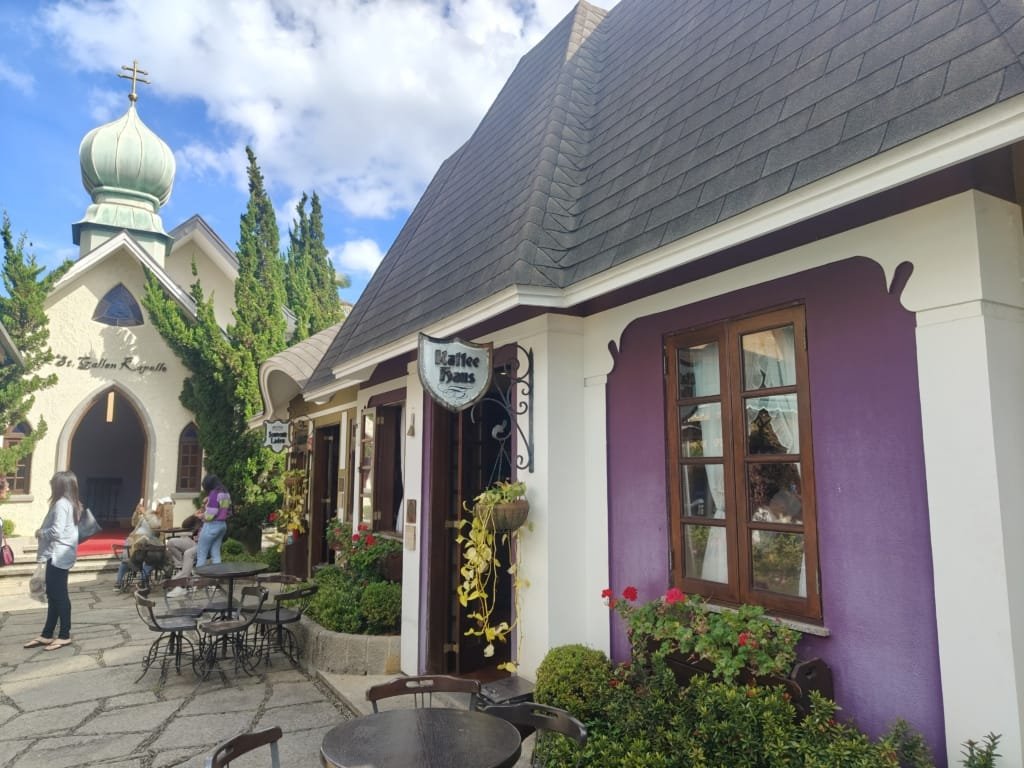 Detalhe da charmosa arquitetura da capela e da Kaffee Haus na Vila St. Gallen, com janelas floridas e mesas de café ao ar livre