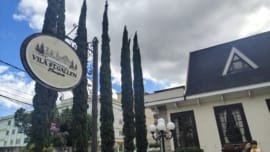 Exterior sign of Vila St. Gallen in Teresópolis, with pine trees in the background and a partly cloudy sky, marking the entrance to the German-inspired complex