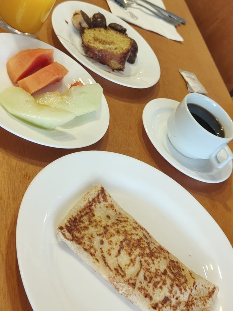 Café da manhã no restaurante do Sesc Alpina com frutas frescas, panqueca, bolo, café e suco de laranja, servido em julho de 2025.
