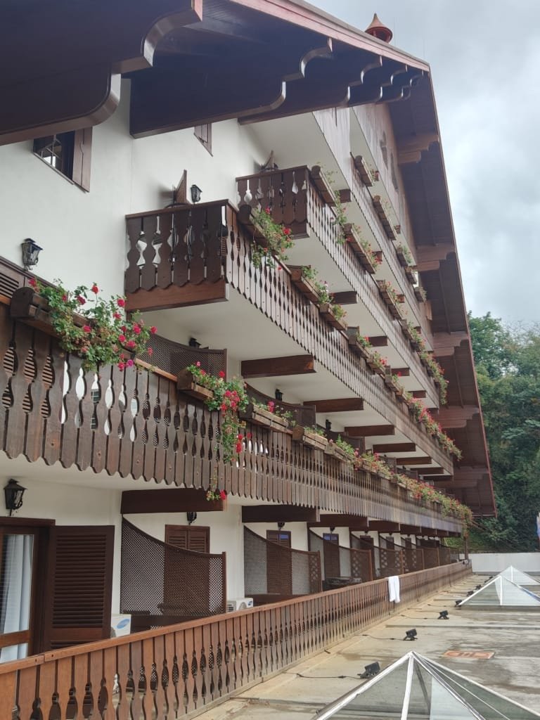 Fachada do Sesc Alpina com varandas decoradas com flores vermelhas e arquitetura alpina típica, registrada em julho de 2025.