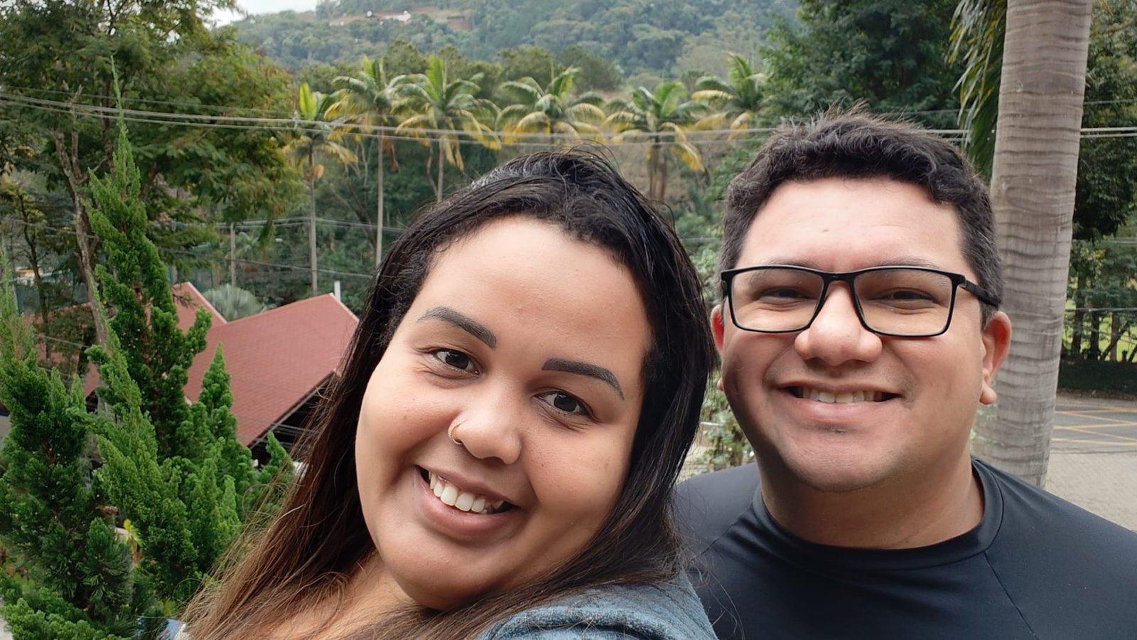 Casal sorridente aproveitando a vista para as montanhas e palmeiras no Sesc Alpina durante viagem em julho de 2025