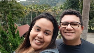 Casal sorridente aproveitando a vista para as montanhas e palmeiras no Sesc Alpina durante viagem em julho de 2025