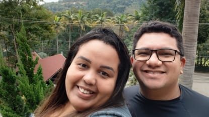 Casal sorridente aproveitando a vista para as montanhas e palmeiras no Sesc Alpina durante viagem em julho de 2025
