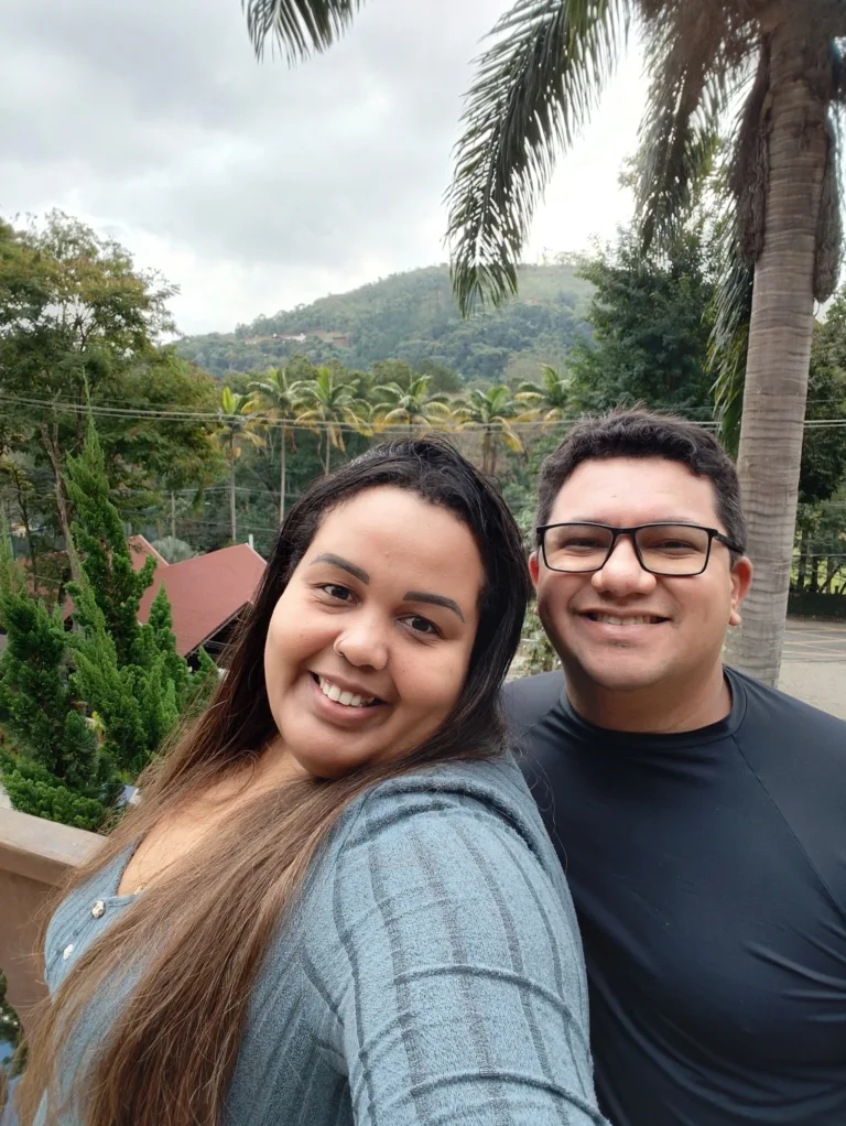 Casal sorridente aproveitando a vista para as montanhas e palmeiras no Sesc Alpina durante viagem em julho de 2025