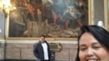 Casal viajando no Palácio de Versalhes durante o Roteiro Europa 2025, sorrindo em frente a uma pintura histórica nas galerias do palácio na França, roteiro de 2 dias em Paris