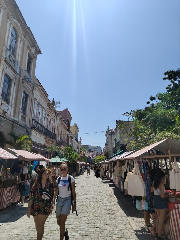 Rua da Feira do Lavradio na Lapa, com barracas de artesanato e visitantes caminhando sob o sol