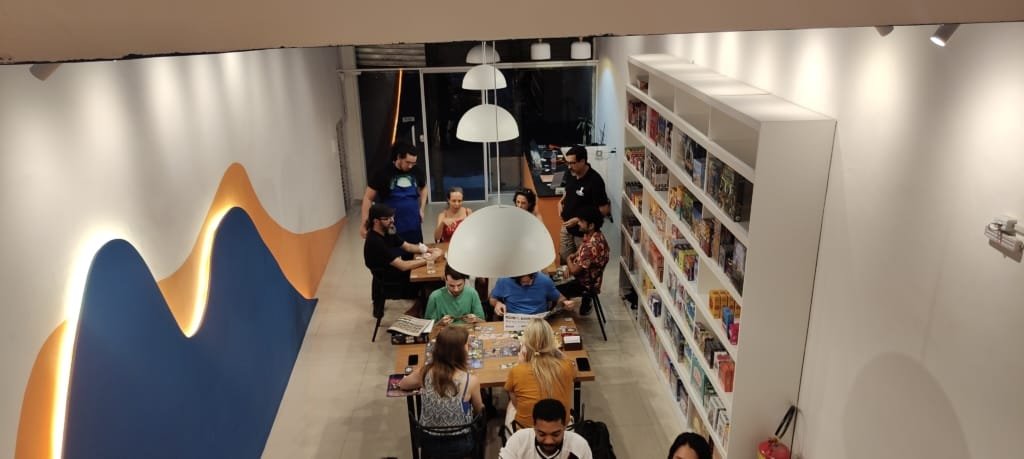 Interior da Luderia Carioca no Flamengo, com visitantes jogando e prateleiras cheias de jogos de tabuleiro, um dos passeios fora do óbvio no Rio de Janeiro para quem busca diversão offline.
