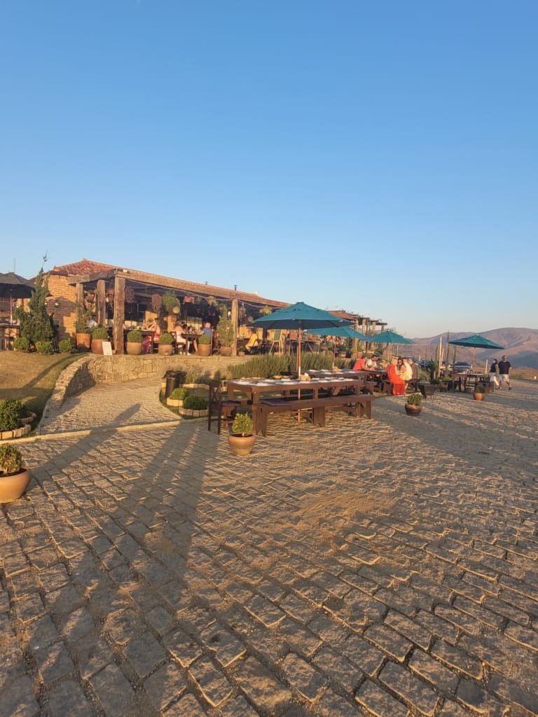 Área externa da Borgo del Vino em Areal com mesas de madeira, guarda-sóis e clima aconchegante durante o pôr do sol