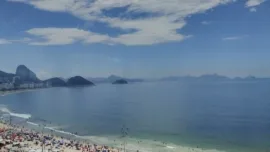 Praia de Copacabana no Rio de Janeiro com orla movimentada, calçadão e mar azul em dia de verão
