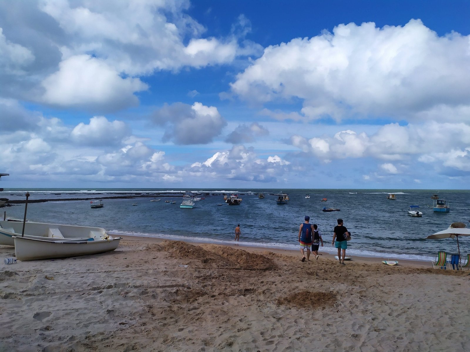 Praia no Nordeste do Brasil com barcos no mar e turistas caminhando na areia
