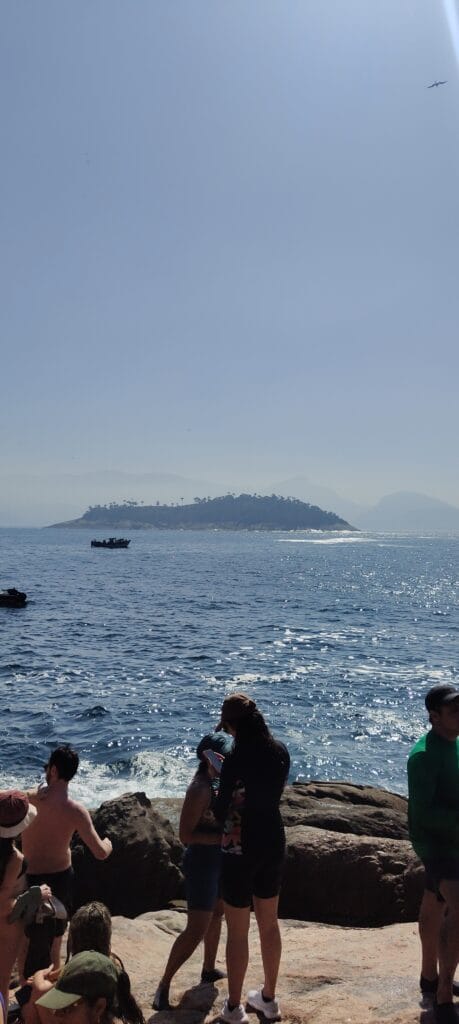 Passeio às Ilhas Cagarras no Rio: barco, trilha, preço e nossa experiência 4 Vista das Ilhas Cagarras a partir da Ilha Comprida, com barco no mar e montanhas do Rio ao fundo.